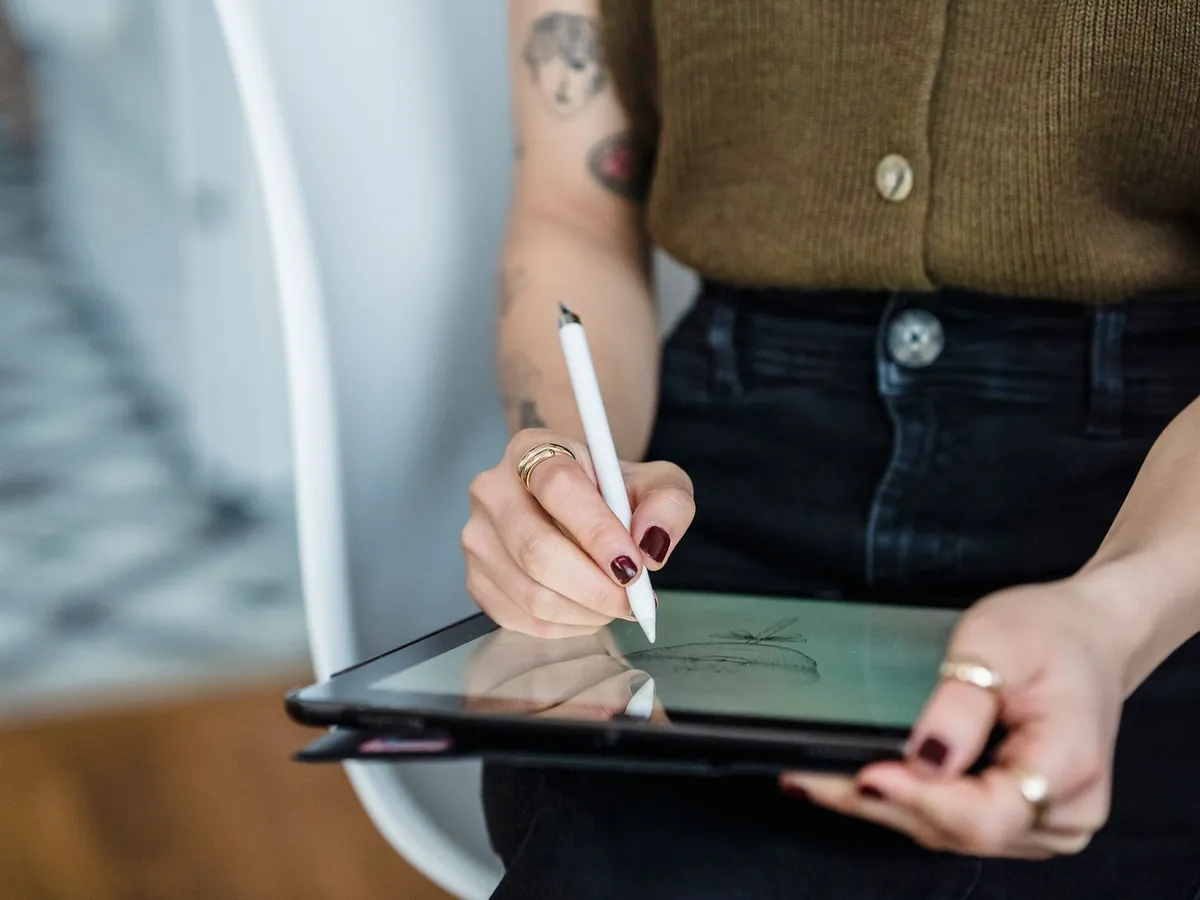 Vrouw tekent met een witte stylus op een tablet die ze op schoot vasthoudt