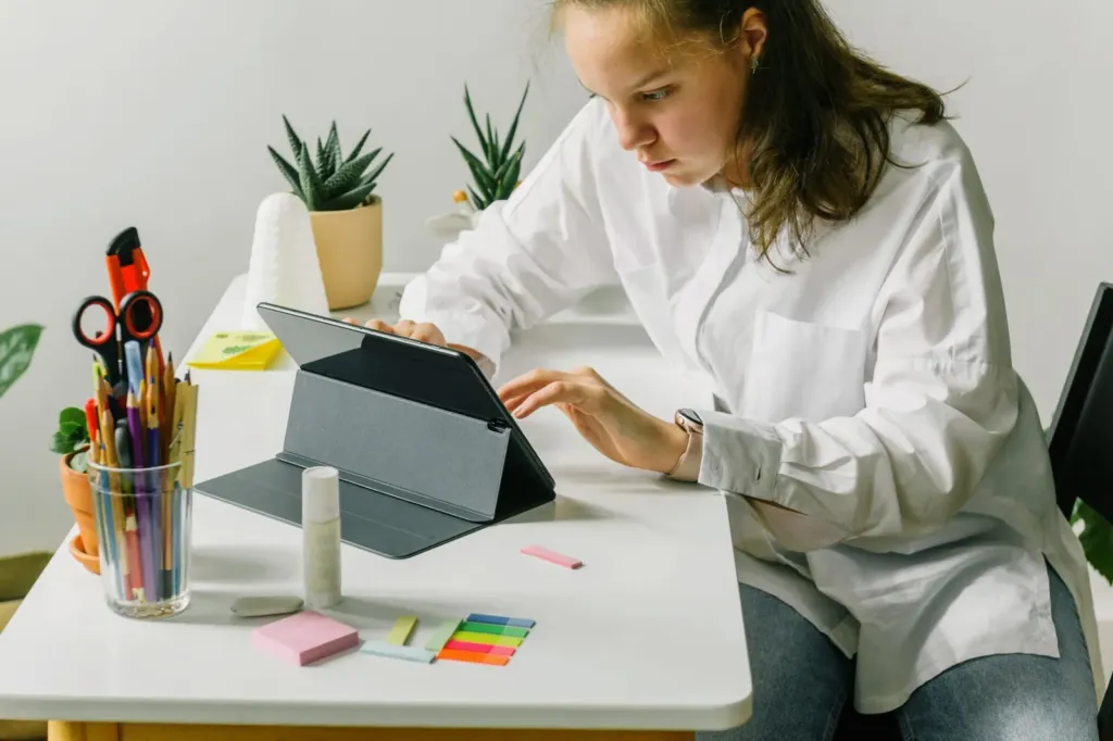 Jonge vrouw werkt aan een bureau op een tablet in een hoes met standaard, met pennen en memoblaadjes