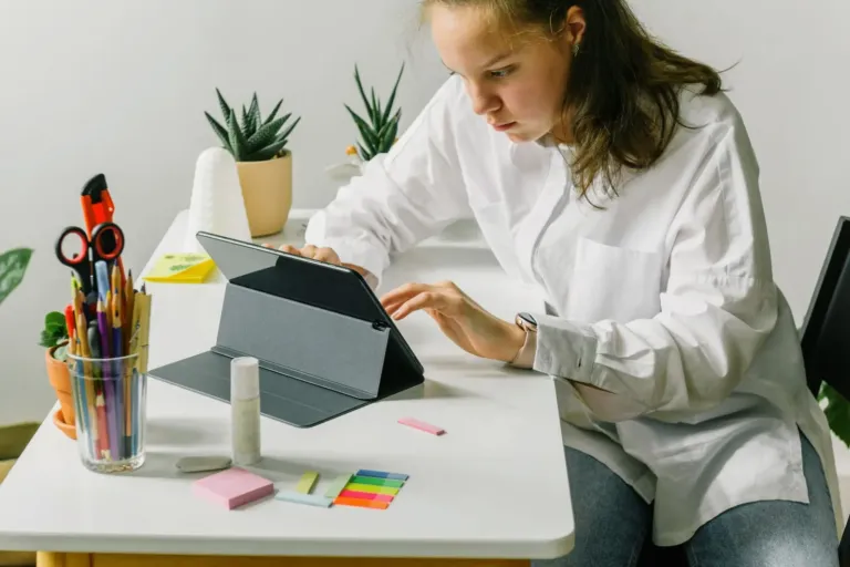 Jonge vrouw werkt aan een bureau op een tablet in een hoes met standaard, met pennen en memoblaadjes