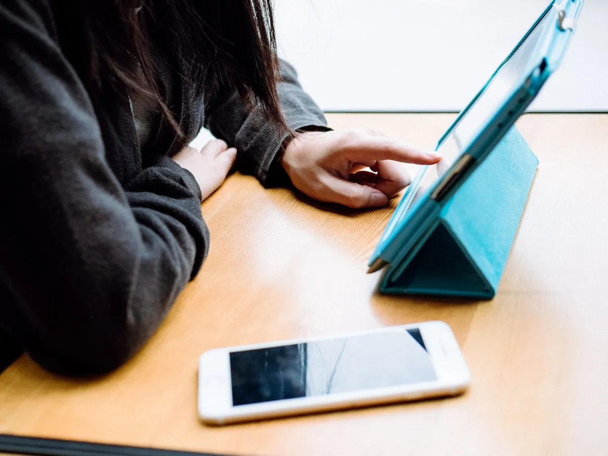 Tablet in een blauwe hoes die als standaard op een houten tafel staat, naast een smartphone