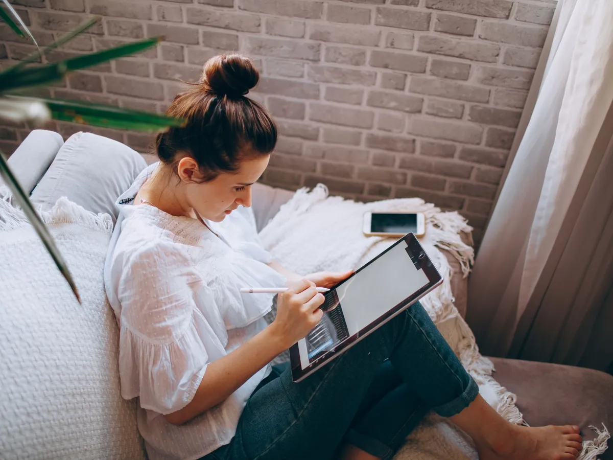 Jonge vrouw zit op de bank en tekent met een stylus op een tablet