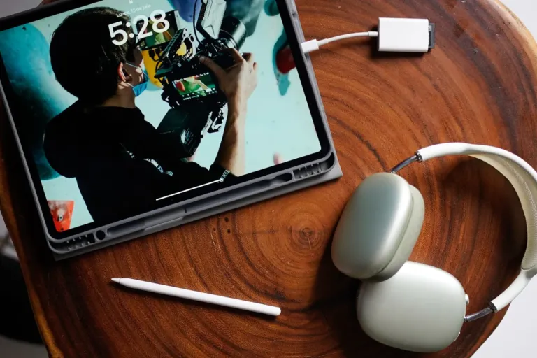 iPad met aangesloten oplaadkabel op een houten tafel, naast een koptelefoon en een Apple Pencil