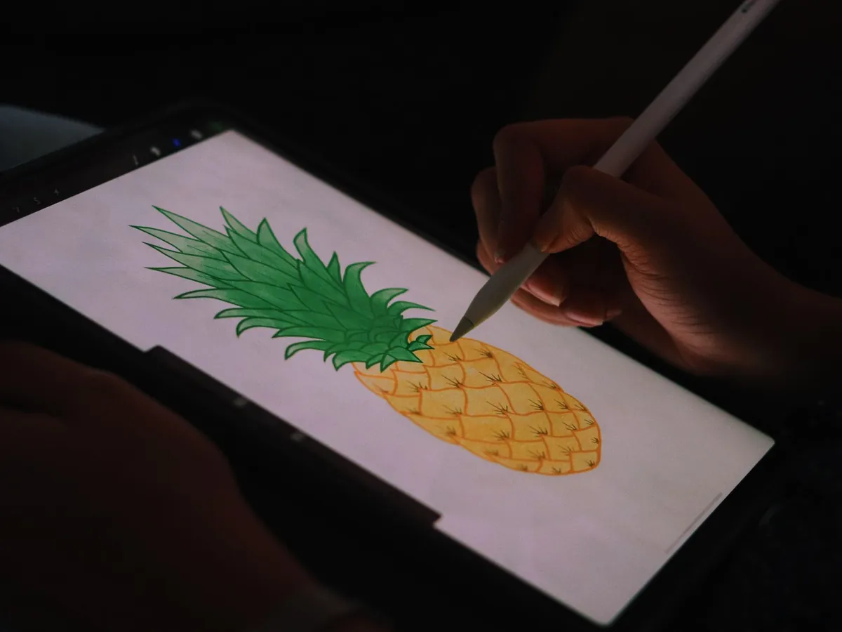 Close-up van een hand die met een stylus een ananas tekent op een tabletscherm