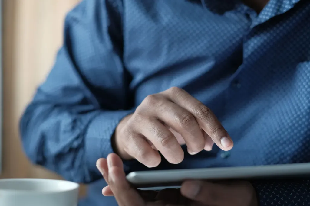 Man tikt met zijn wijsvinger op het scherm van een tablet die hij in zijn hand houdt