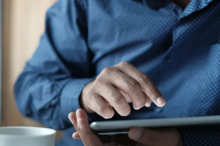 Man tikt met zijn wijsvinger op het scherm van een tablet die hij in zijn hand houdt
