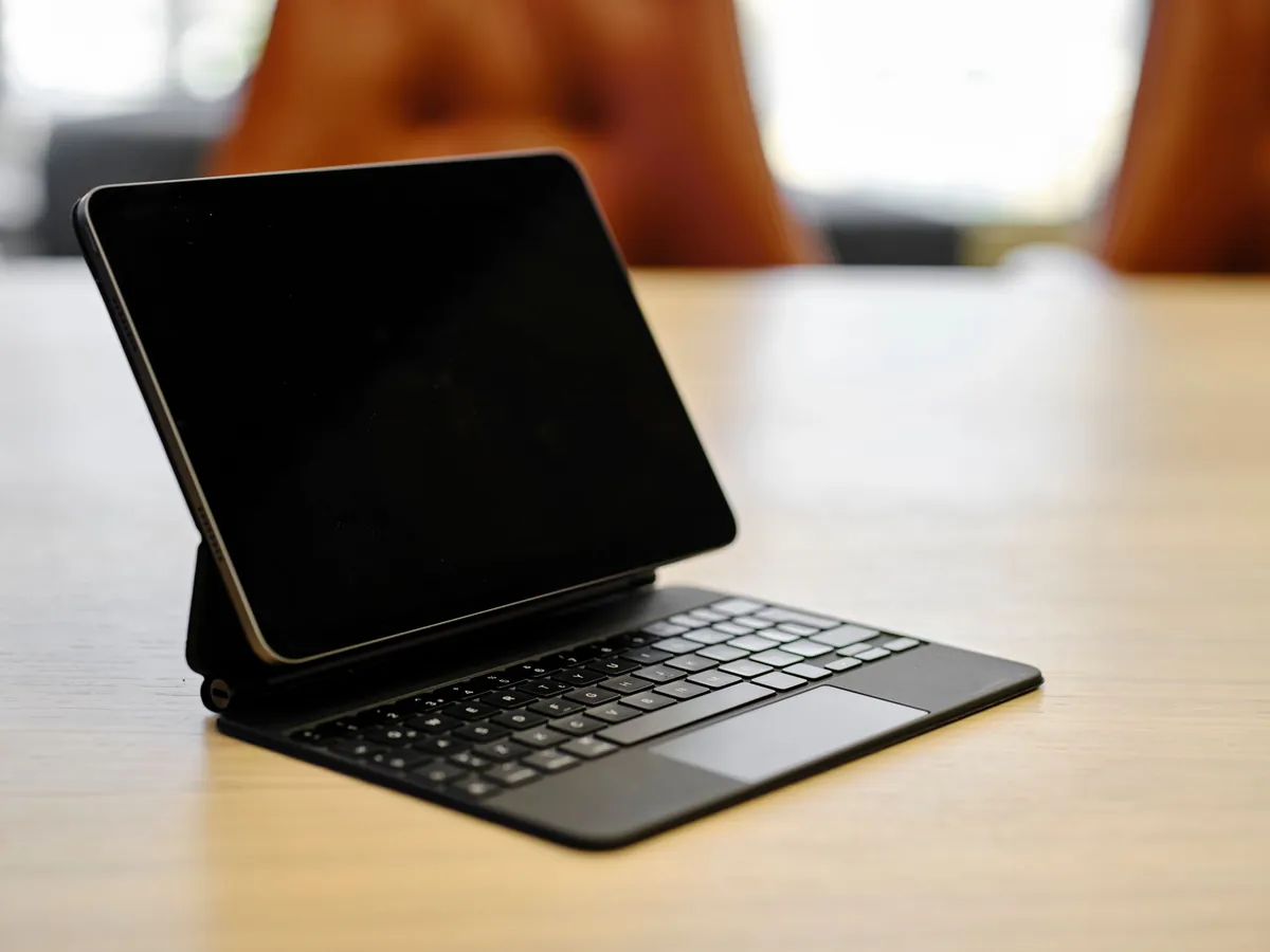 Tablet zwevend boven een zwart toetsenbord met trackpad op een houten tafel