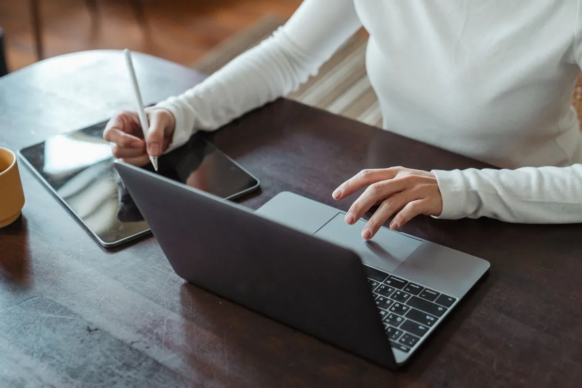 Vrouw werkt op een laptop en schrijft met een pen op een tablet ernaast