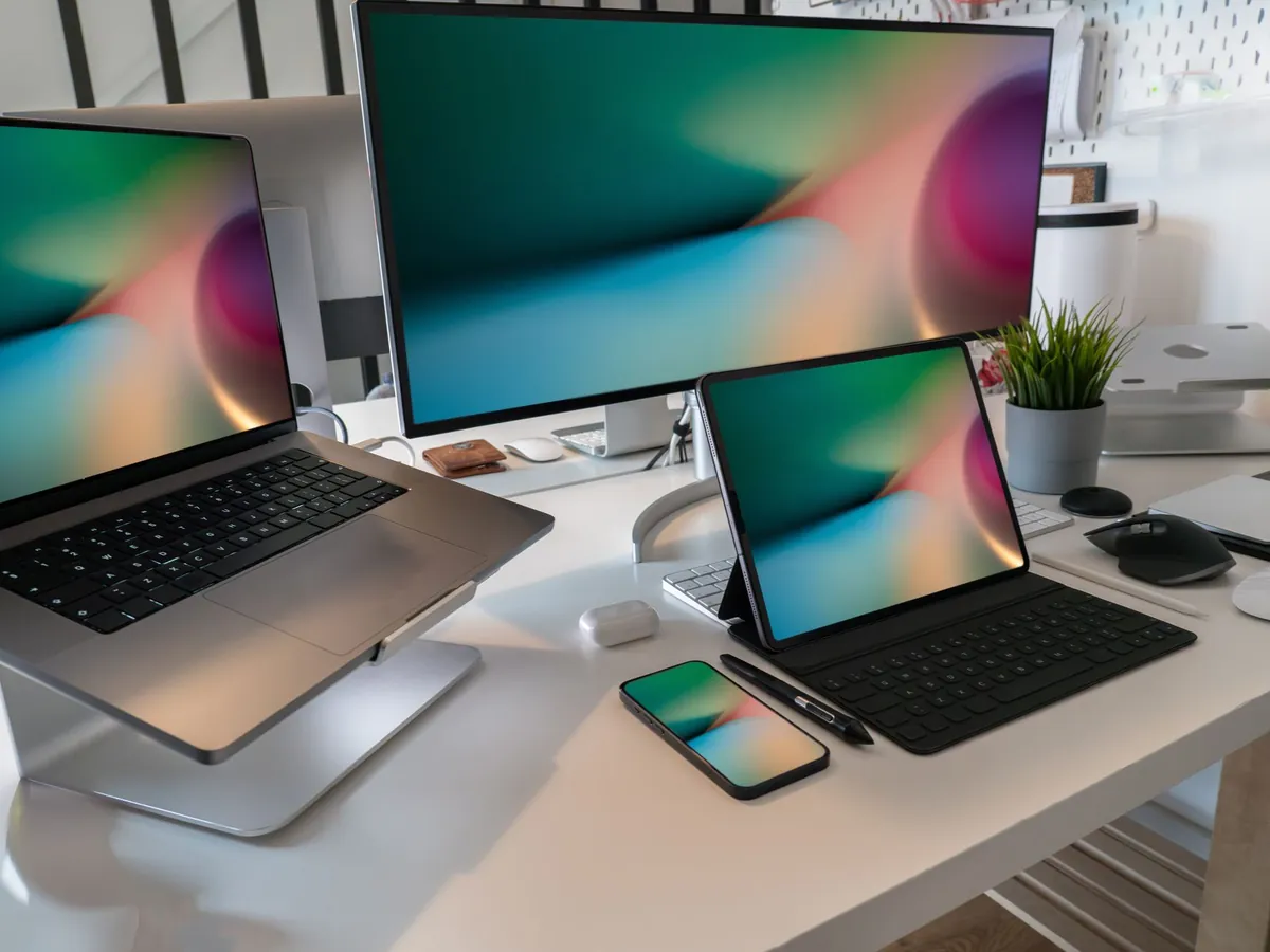 Werkplek met laptop, monitor, tablet met toetsenbord en smartphone op een wit bureau
