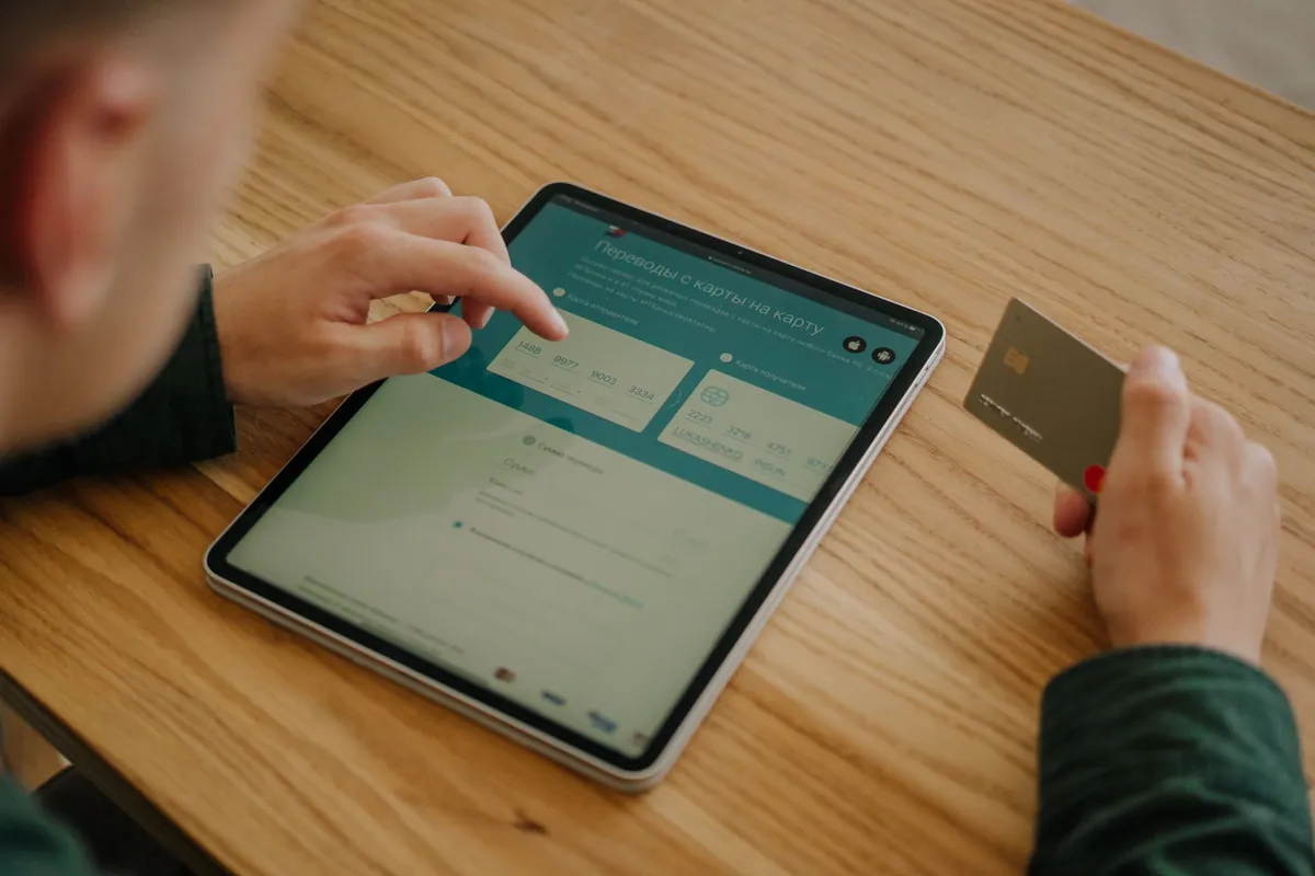 Iemand aan een houten tafel met een tablet en een betaalpas in de hand