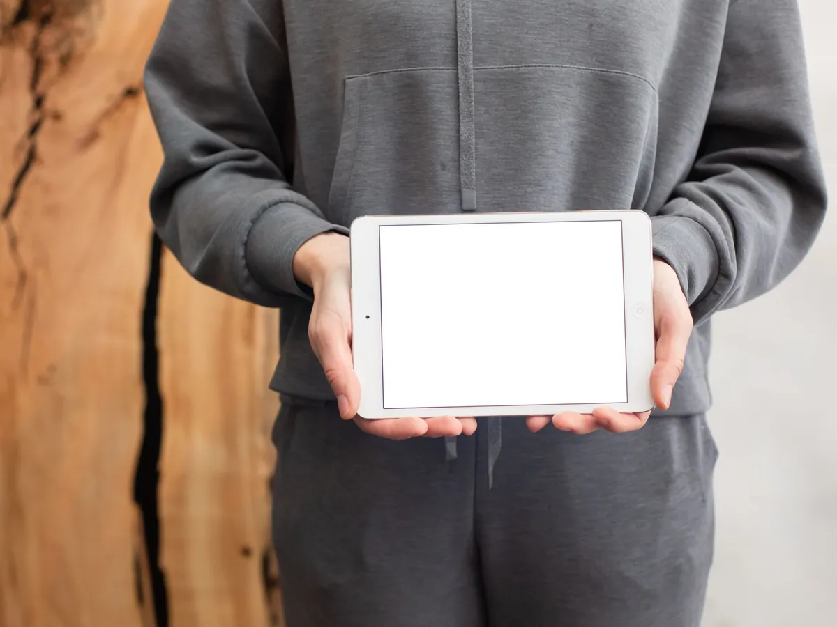 Persoon in grijze trui houdt een witte tablet met een leeg scherm voor zich