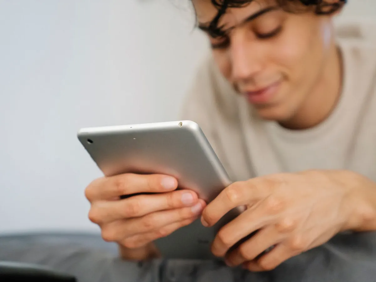 Glimlachende tiener ligt op bed en gebruikt een zilveren tablet