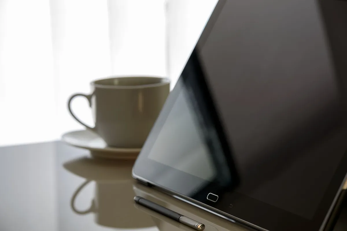 Tablet met zwart scherm op een glanzend bureau naast een kop koffie