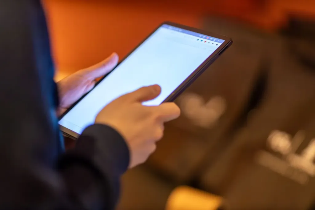 Handen die een tablet vasthouden en het scherm aanraken in een warm verlichte kamer