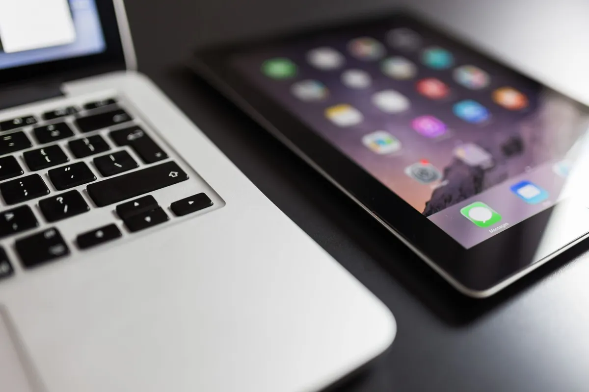 Tablet met app-iconen naast een opengeklapte laptop op een donker bureau